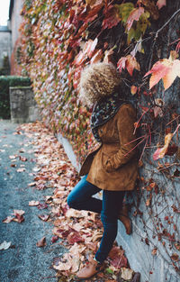 Side view of woman with curly hair leaning on ivy covered wall during autumn