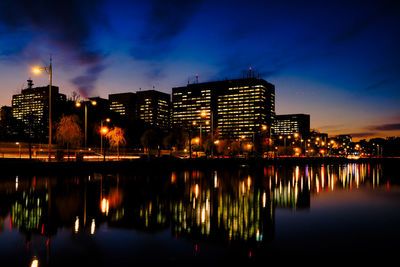 Illuminated buildings by river against sky at night