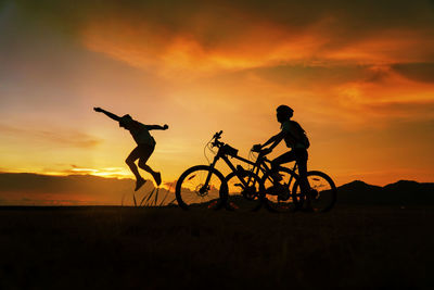 Silhouette man riding bicycle on field against sky during sunset