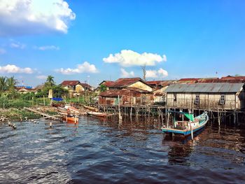 Boats in river by buildings against blue sky