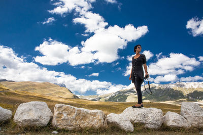 Full length of young woman standing on rock against sky