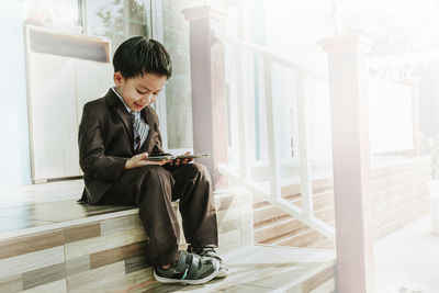 Boy looking through window while sitting on floor