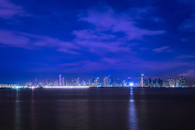 Illuminated buildings by sea against sky at night