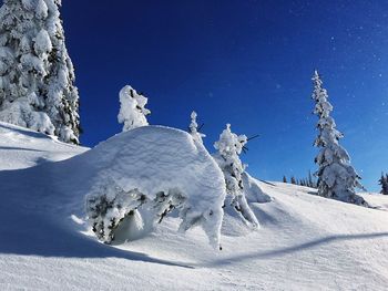 Low angle view of frozen trees on snow covered hill against clear blue sky