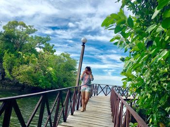 Woman walking on footbridge against sky