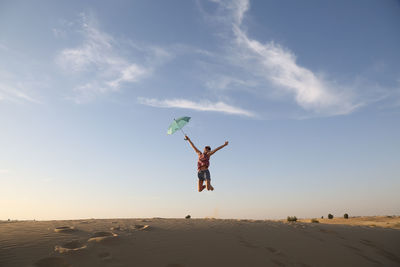 Girl jumping on sand against sky