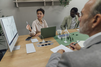Businesswoman explaining over computer to colleagues at table in office