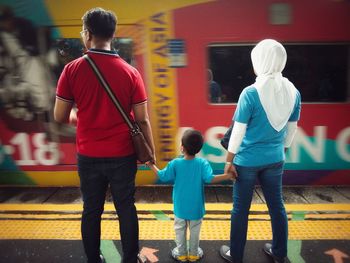 Rear view of family holding hands while standing at railroad station platform