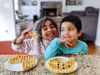 Happy siblings eating waffles at home