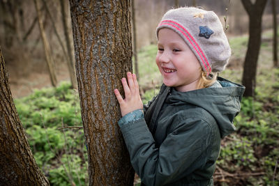 Portrait of cute girl standing by tree trunk