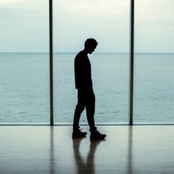 Side view of man standing with sea seen through window