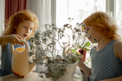 Redhead girl with sister watering plant at home