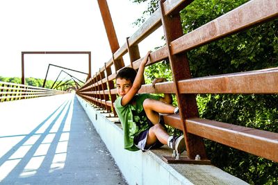 Portrait of boy sitting on railing at bridge