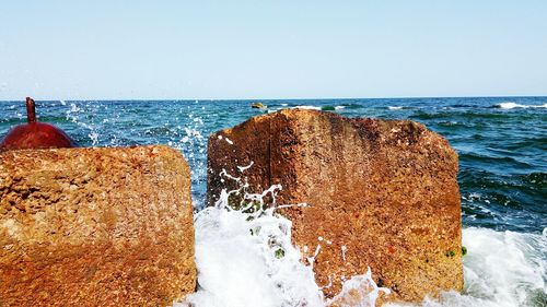 Sea waves splashing on rock against clear sky