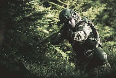 Soldier aiming gun while standing in forest