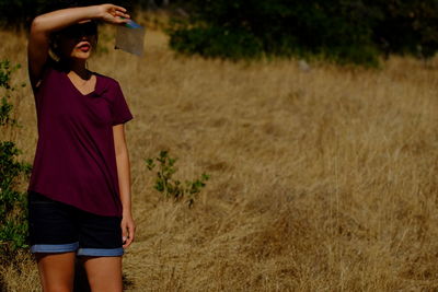 Young woman shielding eyes while standing on field