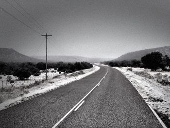 Road leading towards landscape against clear sky