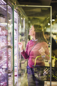 Mature woman looking in refrigerator while shopping at grocery store
