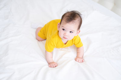 Healthy asian baby girl 5 months in yellow bodysuit on bed on white bedding