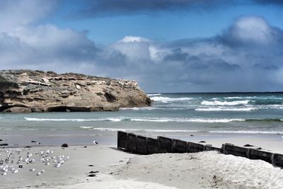 Scenic view of sea by rock formations against cloudy sky