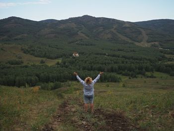 Rear view of woman with arms raised standing on field