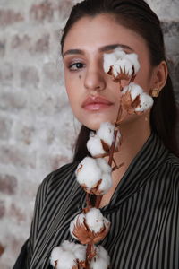 Portrait of young woman holding flower by wall