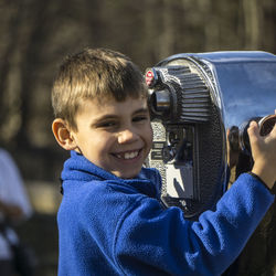 Portrait of smiling boy standing by coin-operated binocular