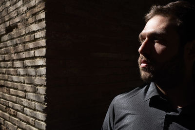 Thoughtful man standing against wall on sunny day