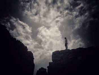 Low angle view of silhouette man standing on cliff against sky