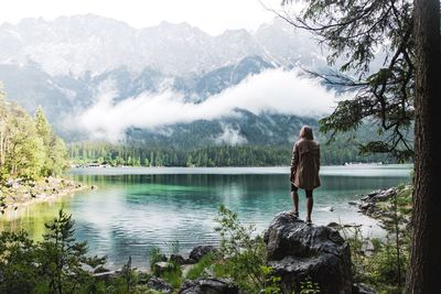 Rear view of man standing by lake against mountains