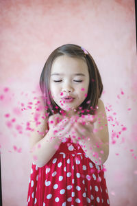Cute girl blowing confetti against pink wall
