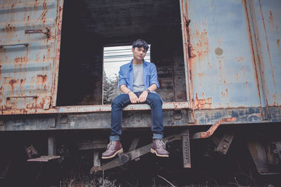 Low angle portrait of sad young man sitting on abandoned freight train