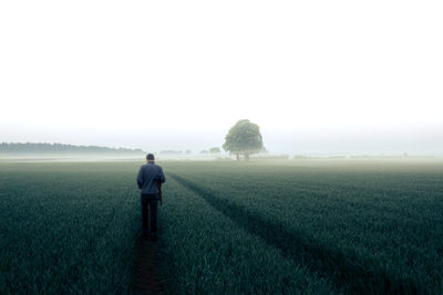 Rear view of man standing on field against clear sky