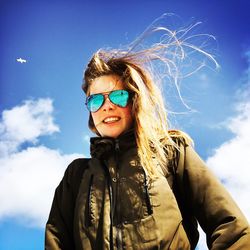 Portrait of young woman wearing sunglasses standing against sky