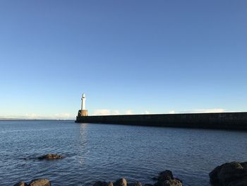 Lighthouse by sea against clear blue sky