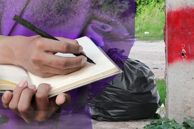 Digital composite image of person writing in book by garbage bags