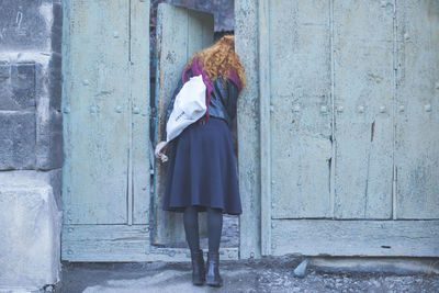 Rear view of woman peeping through old door