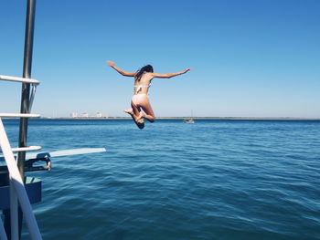 Rear view of young woman jumping in sea against clear sky