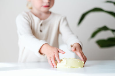 Girl, toddler hands playing with yellow sticky slime indoors at home on white table