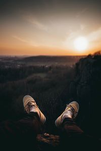 Low section of man sitting on mountain at sunset