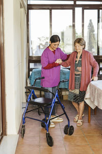 Young caregiver helping senior woman to walk at home