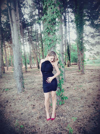Young woman standing by tree in forest