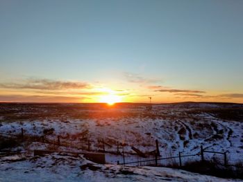 Snow covered landscape against sky during sunset