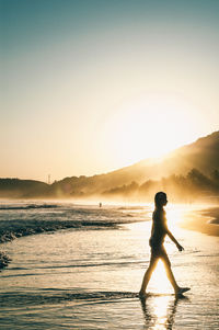 Side view of silhouette woman walking on shore against clear sky during sunset