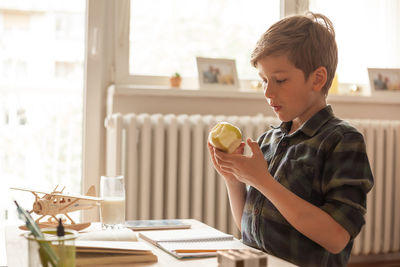 Cute boy eating a fresh apple while studying during home schooling in the living room.