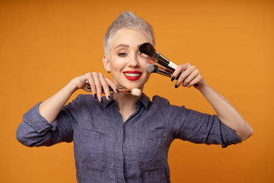 Portrait of smiling woman with make-up brushes against orange background