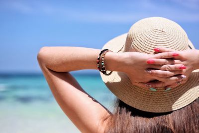 Woman wearing hat with hands behind head at beach 