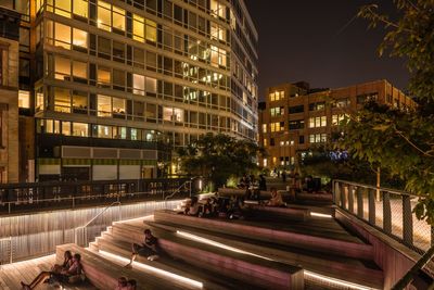 People sitting by building in high line park at night