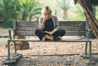 Woman reading book while sitting on bench in park