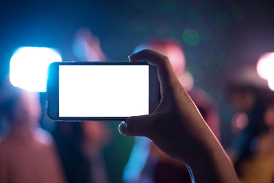 Cropped hand holding mobile phone at night